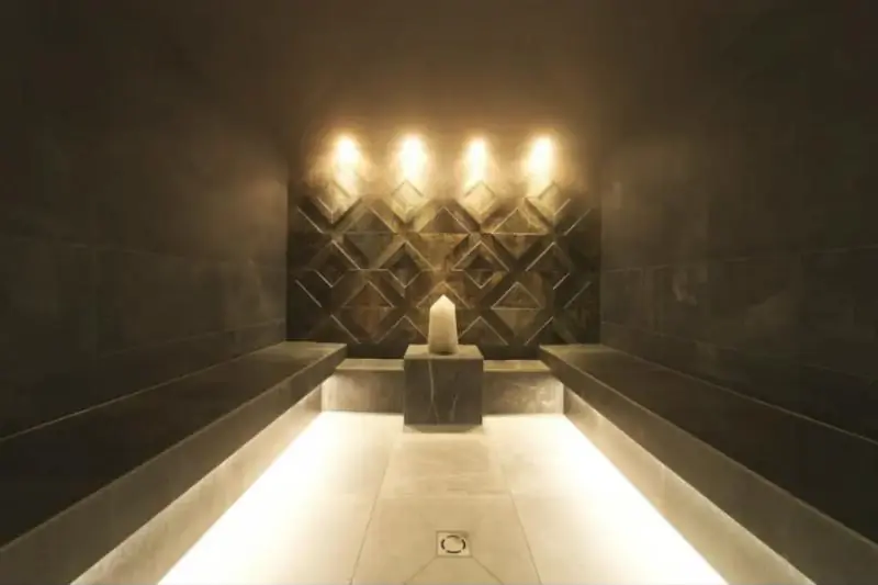 Hammam en pierre sombre avec banquettes éclairées et lumière tamisée