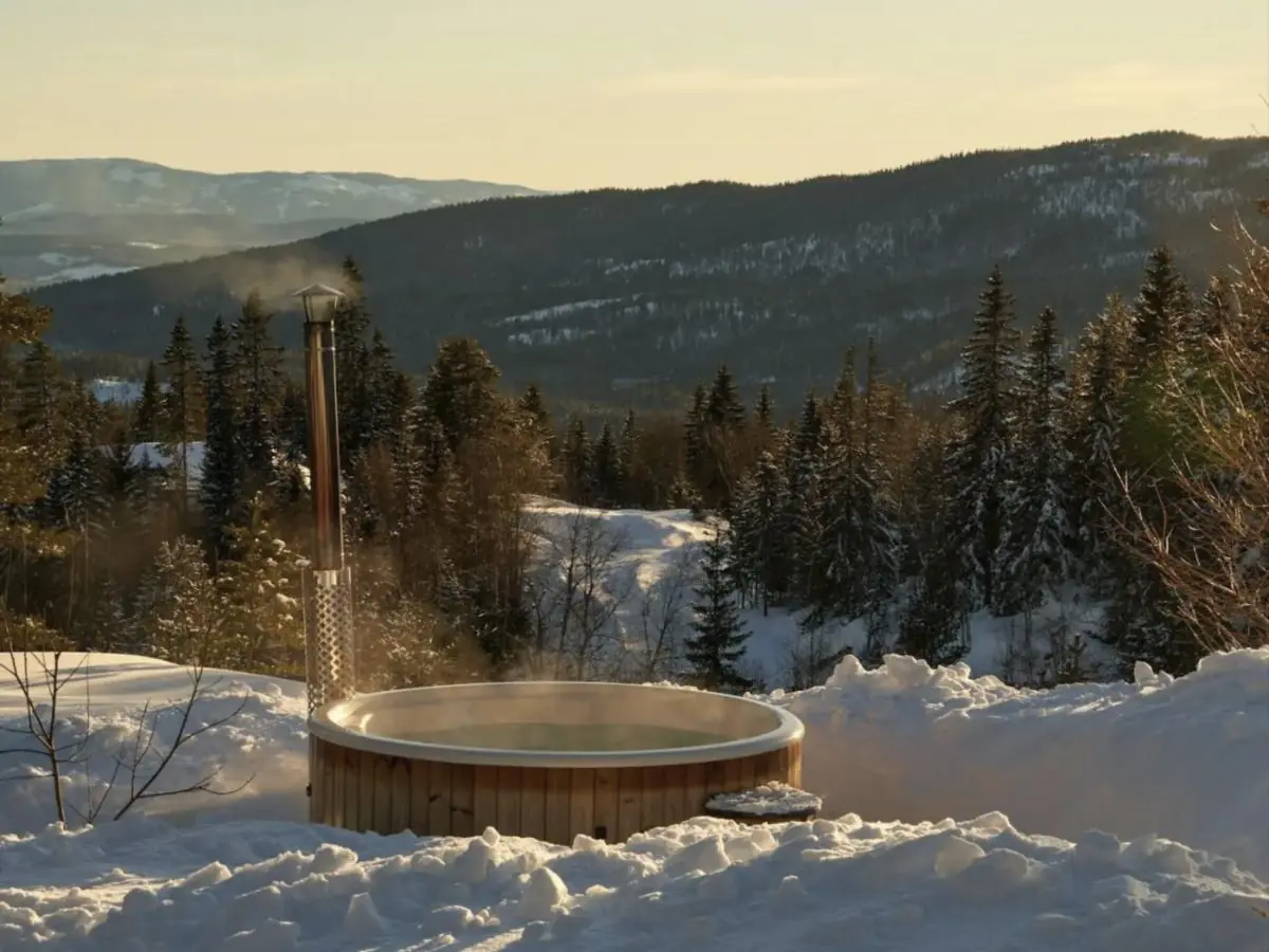Bain nordique fumant face à un paysage de collines enneigées au soleil couchant
