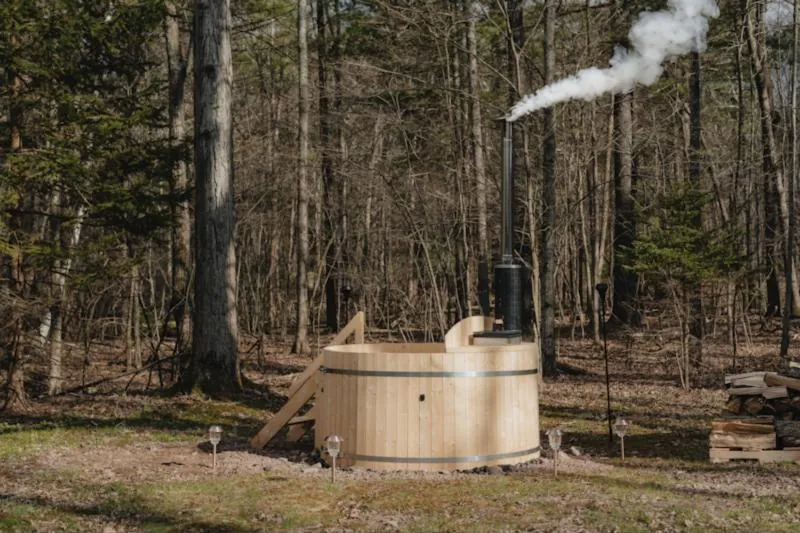 Bain nordique en bois clair dans un sous-bois, la cheminée du poêle fumant