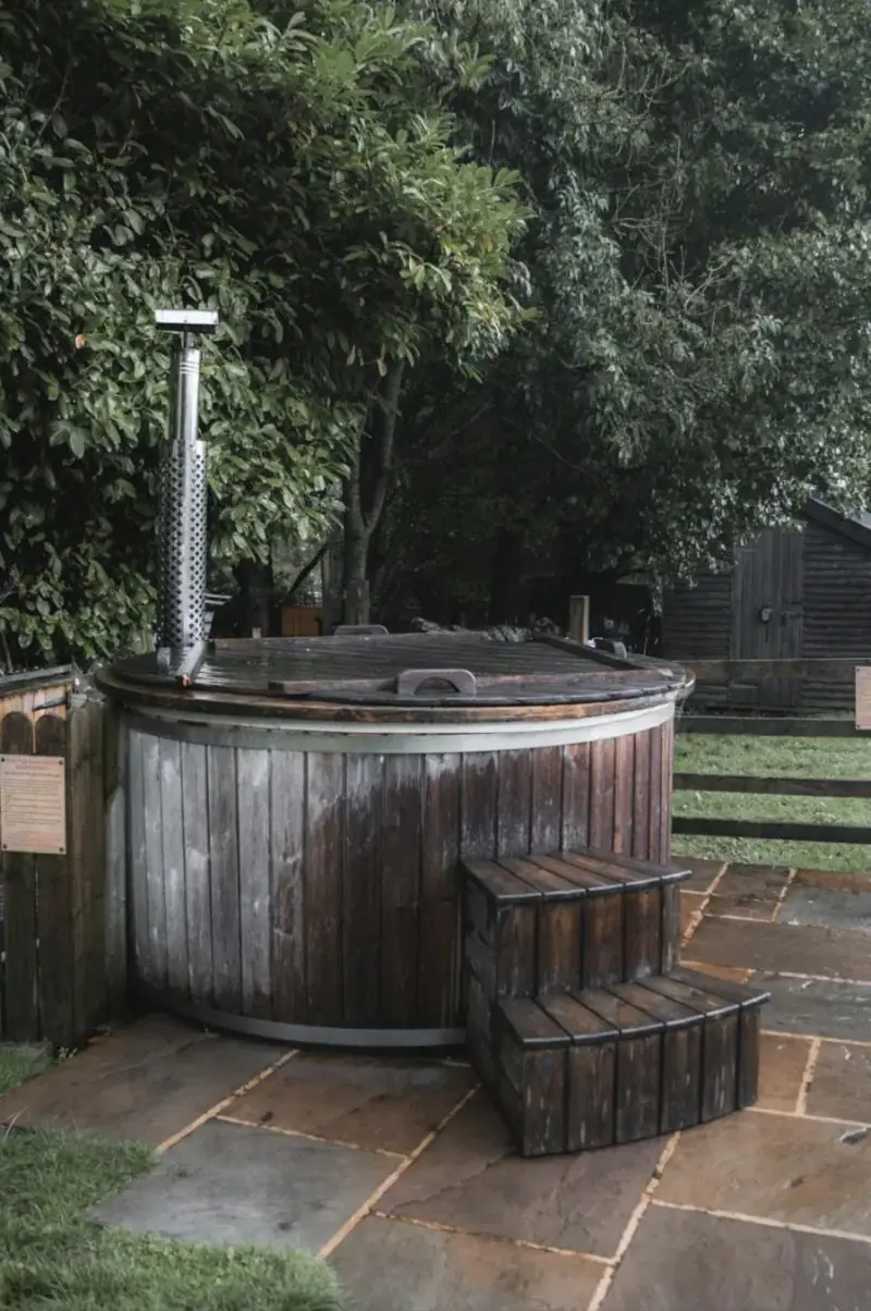 Bain nordique en bois avec cheminée de poêle, posé sur un dallage en pierre dans un jardin