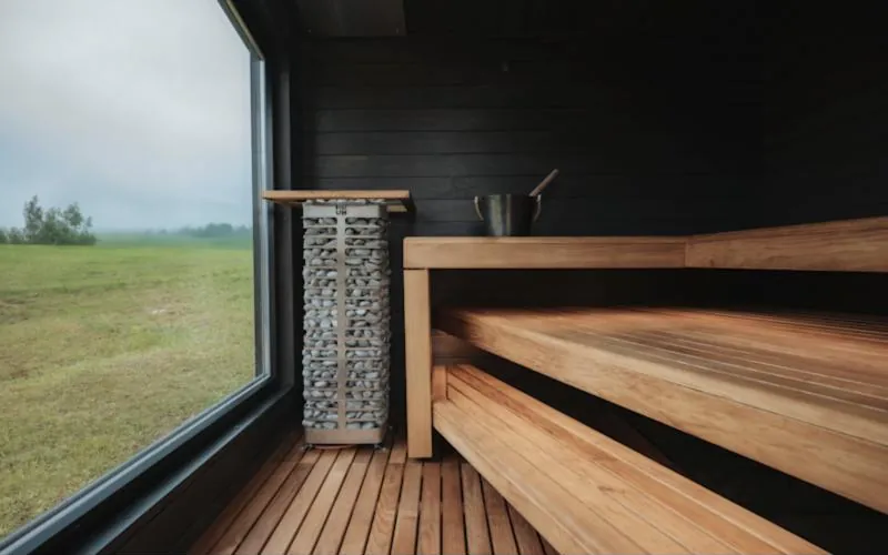 Intérieur de sauna en bois sombre avec poêle à pierres et grande fenêtre sur la campagne
