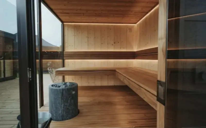 Sauna moderne en bois clair avec éclairage indirect et poêle en pierre