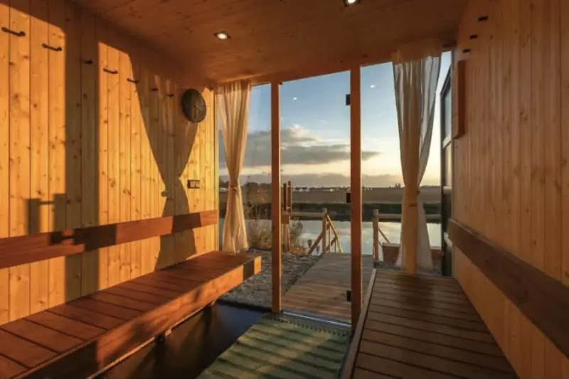 Sauna en bois ouvert sur un étang au coucher du soleil