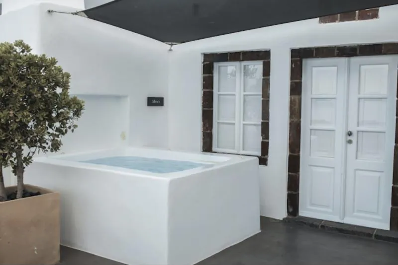 Spa maçonné blanc sur une terrasse ombragée, devant une façade aux volets blancs