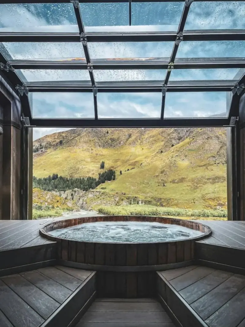 Bain bouillonnant en bois sous une verrière ouverte sur la montagne