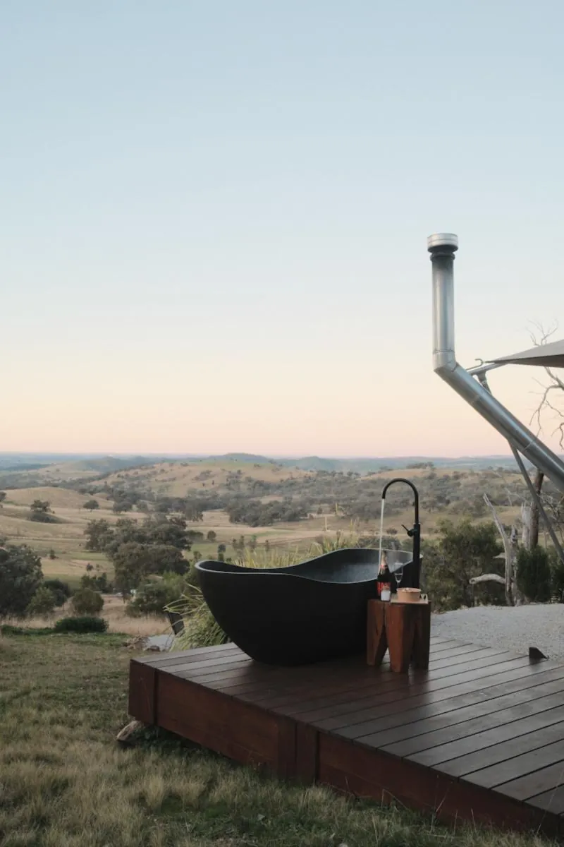 Baignoire îlot noire sur une terrasse en bois face aux collines au coucher du soleil